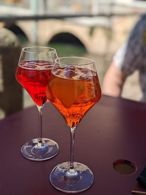 two wine glasses of orange and red liquid on a purple table
